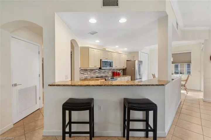 Kitchen with backsplash, a kitchen breakfast bar, light stone countertops, appliances with stainless steel finishes, and kitchen peninsula