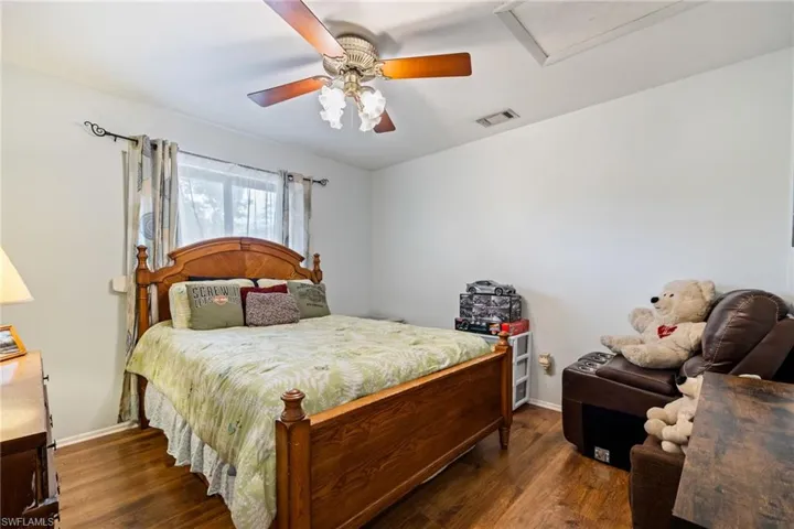 Bedroom featuring a ceiling fan, visible vents, attic access, and dark wood finished floors
