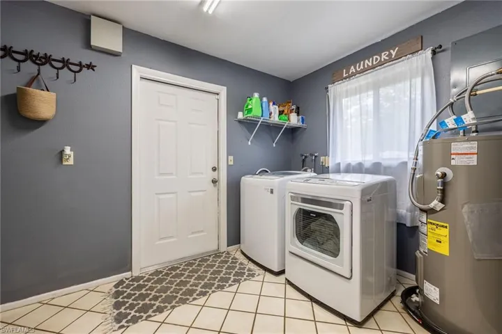 Laundry room with light tile patterned flooring, washer and clothes dryer, electric water heater, and laundry area
