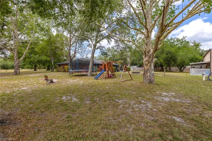 View of yard featuring a trampoline, a playground, and fence