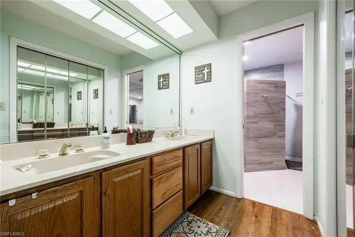 Main bathroom with double vanity, a sink, a tile shower, and wood finished floors