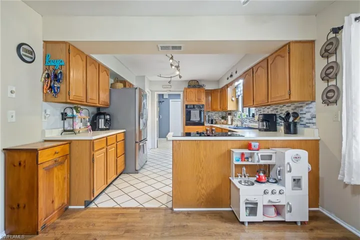 Kitchen with tasteful backsplash, wall oven, visible vents, a peninsula, and brown cabinets