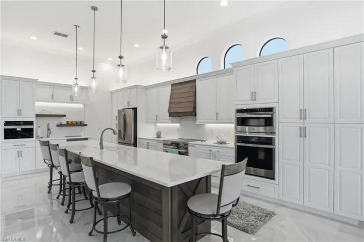 Kitchen featuring stainless steel appliances, a large island with sink, tasteful backsplash, light stone countertops, and ornamental molding