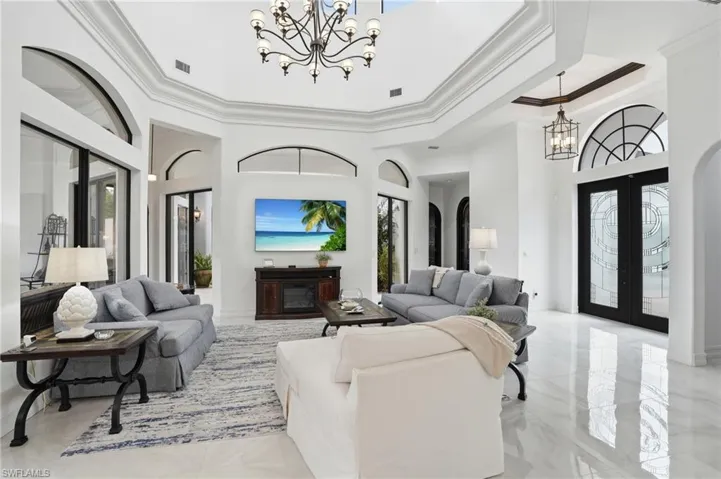 Living area featuring a chandelier, french doors, ornamental molding, a high ceiling, and arched walkways