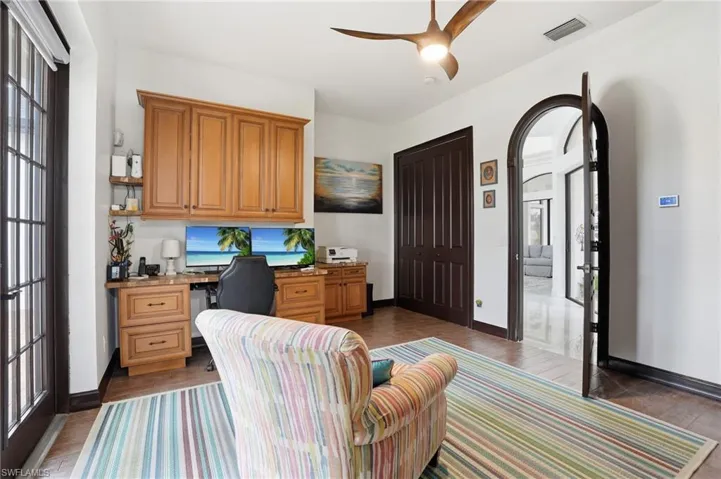 Office space featuring ceiling fan, built in desk, arched walkways, and dark wood-style flooring