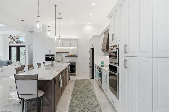 Two tone kitchen with a kitchen bar, two tone cabinets, light stone counters, french doors, and a large island