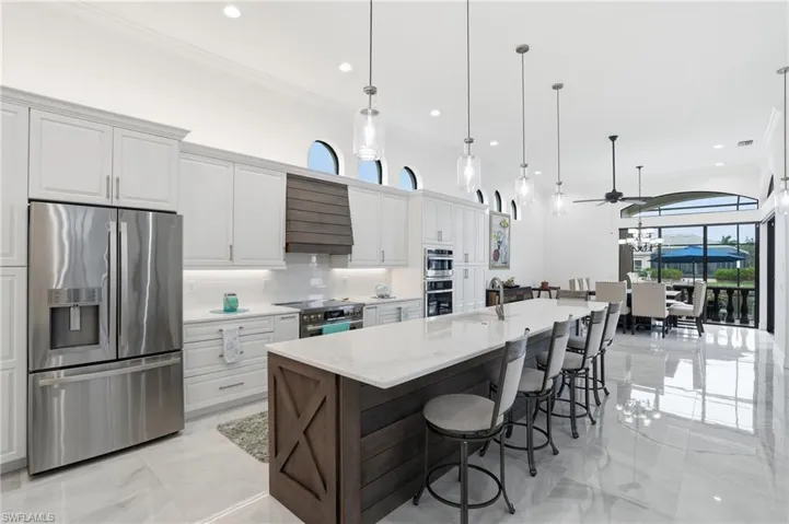 Kitchen with stainless steel appliances, dual tone cabinets, light stone countertops, a large island, and ornamental molding