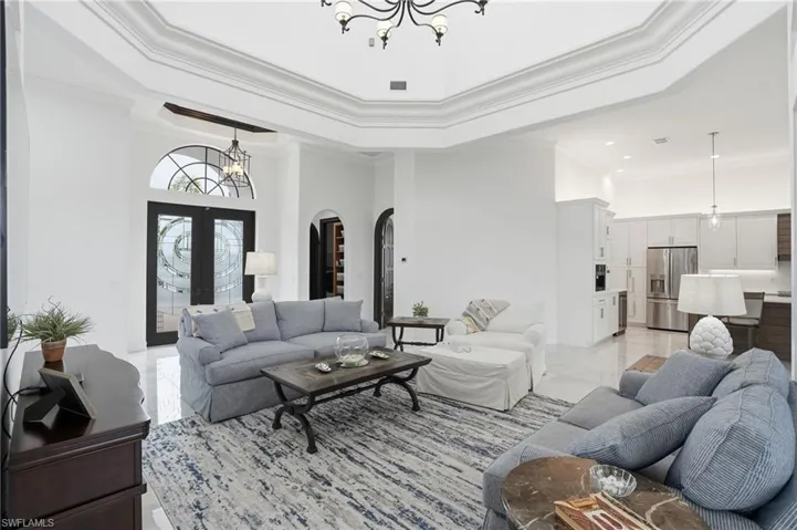 Living room featuring a chandelier, a high tray ceiling, arched walkways, french doors, and ornamental molding