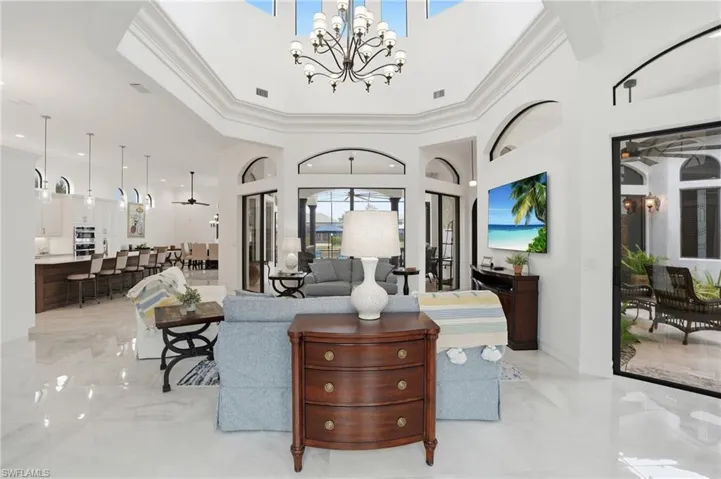 Living area with light marble finish flooring, ornamental molding, suspended lighting, and a high ceiling