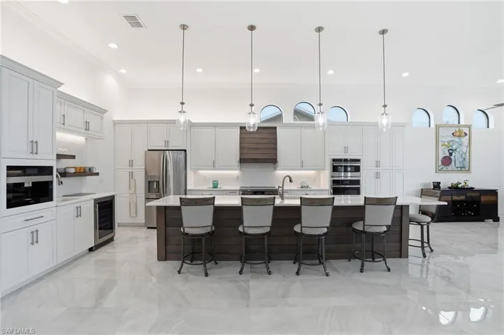 Kitchen with a breakfast bar area, ornamental molding, two tone cabinetry, stainless steel appliances, and a large island with sink