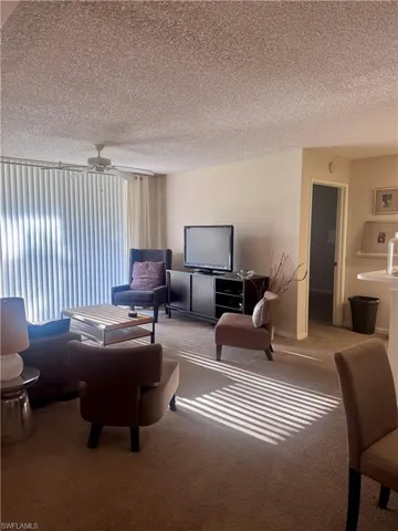 Living room featuring a ceiling fan, a textured ceiling, and carpet