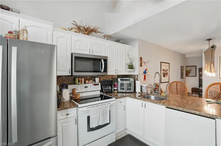 Kitchen featuring appliances with stainless steel finishes, tasteful backsplash, white cabinets, a peninsula, and dark stone counters