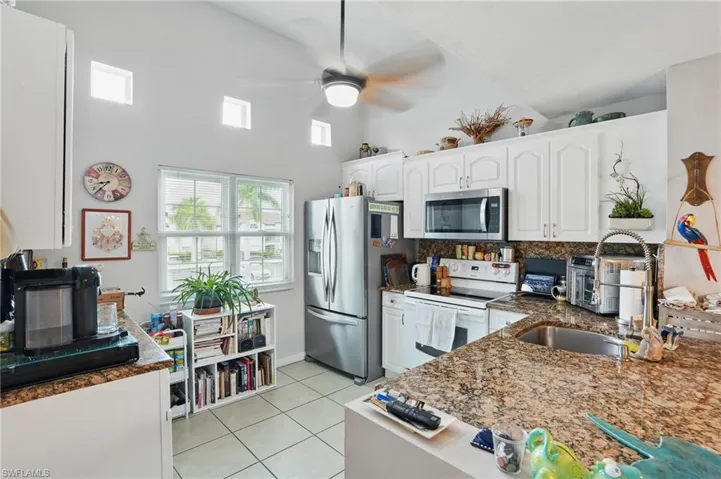 Kitchen with stainless steel appliances, light tile patterned floors, white cabinets, ceiling fan, and decorative backsplash