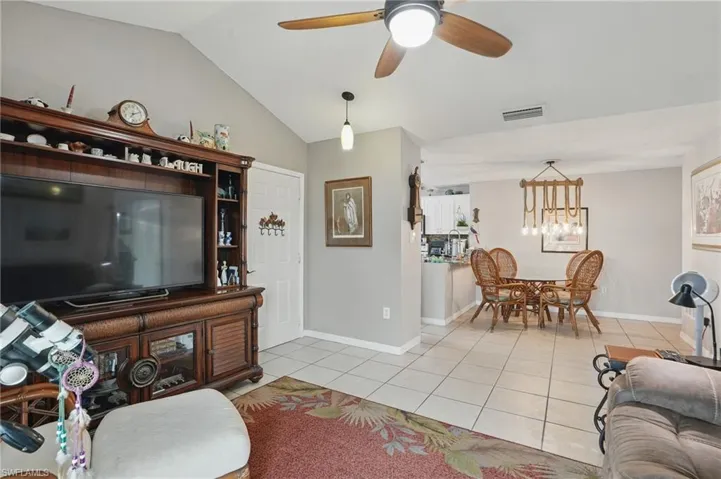 Living room with light tile patterned flooring, vaulted ceiling, ceiling fan, and a chandelier