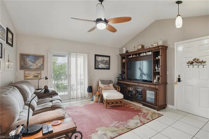 Living room featuring a ceiling fan, vaulted ceiling, and light tile patterned floors