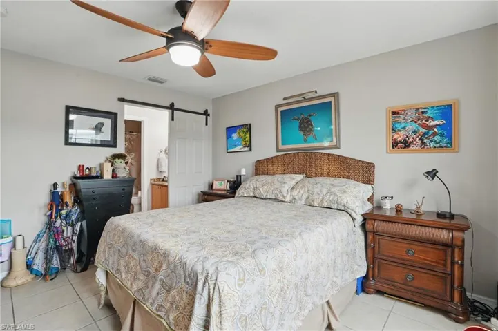Bedroom featuring light tile patterned floors, a barn door, ensuite bath, and a ceiling fan