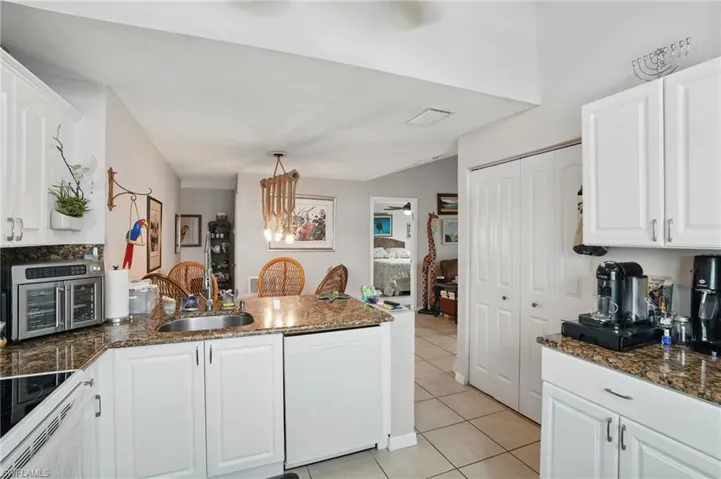 Kitchen with white dishwasher, light tile patterned floors, a peninsula, white cabinets, and hanging light fixtures