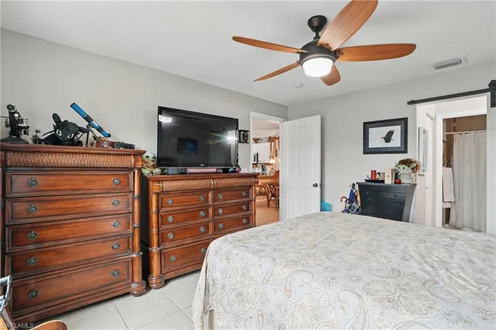 Bedroom featuring light tile patterned flooring, a barn door, and a ceiling fan