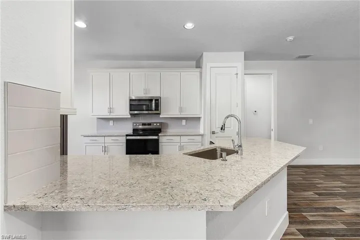 Kitchen featuring appliances with stainless steel finishes, white cabinets, sink, dark hardwood / wood-style floors, and light stone countertops