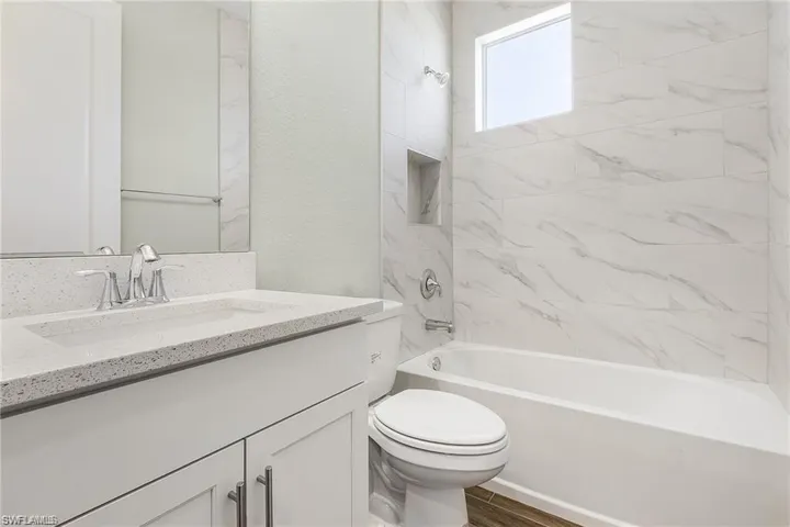 Full bathroom with vanity, tiled shower / bath combo, toilet, and wood-type flooring