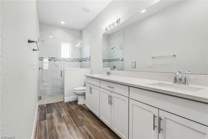 Bathroom with toilet, an enclosed shower, wood-type flooring, and dual bowl vanity
