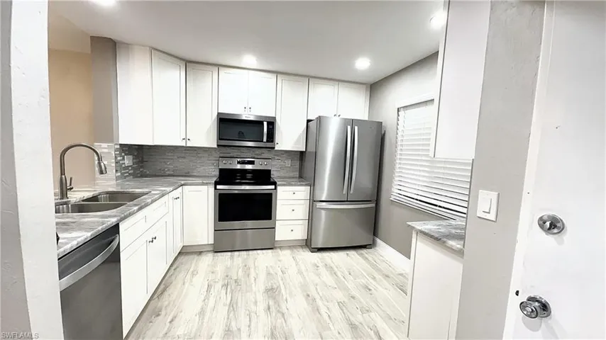 Kitchen with white cabinetry, light hardwood / wood-style flooring, appliances with stainless steel finishes, sink, and tasteful backsplash