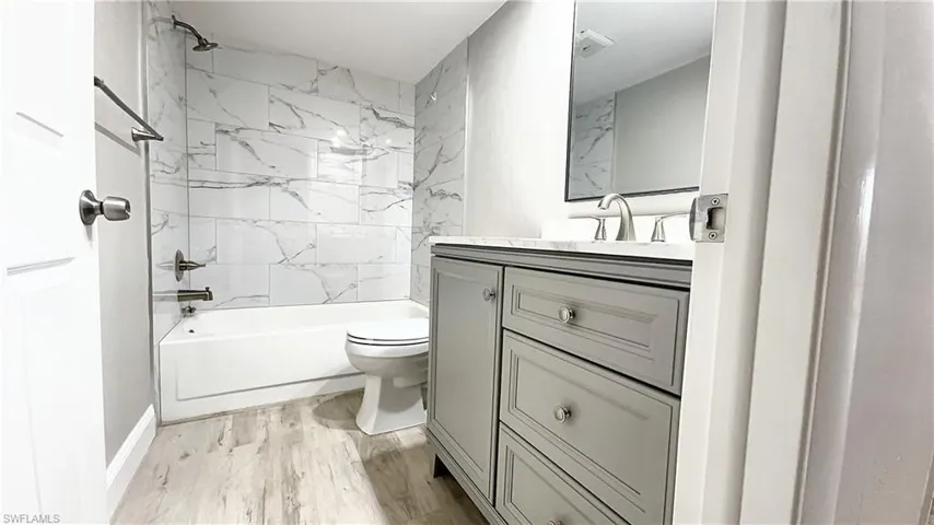 Full bathroom with wood-type flooring, tiled shower / bath, vanity, and toilet