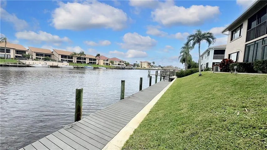 View of dock with central AC, a water view, and a lawn