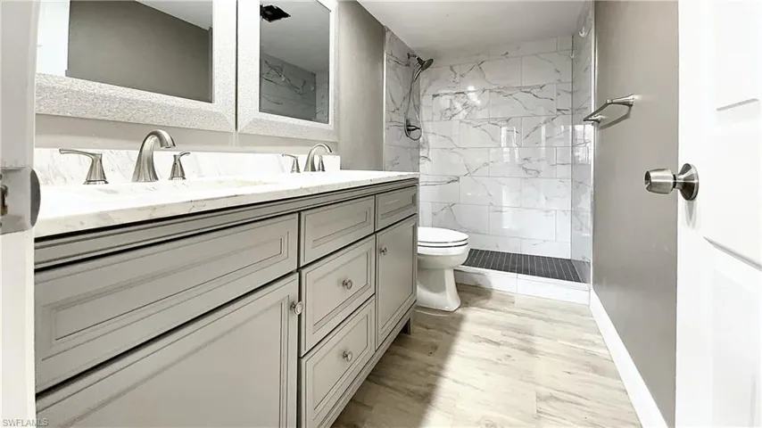 Bathroom featuring tiled shower, hardwood / wood-style flooring, vanity, and toilet
