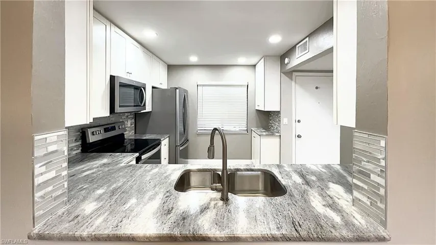 Kitchen featuring backsplash, appliances with stainless steel finishes, sink, and white cabinetry