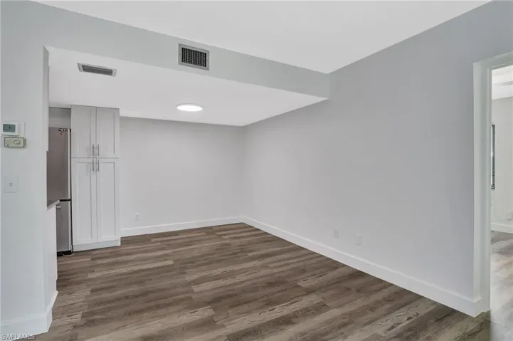 Unfurnished room featuring dark wood-type flooring, visible vents, and baseboards