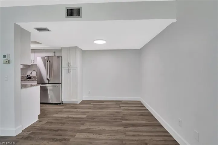 Kitchen featuring dark wood-type flooring, freestanding refrigerator, visible vents, and baseboards