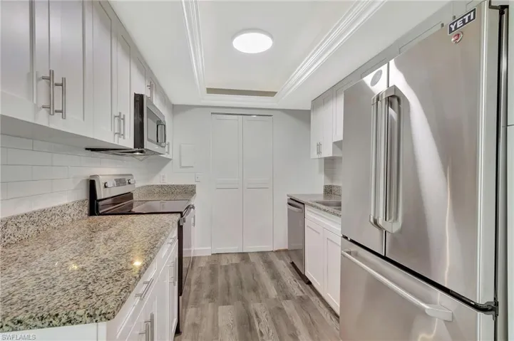 Kitchen with white cabinets, stainless steel appliances, a raised ceiling, decorative backsplash, and light wood-style flooring