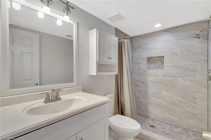 Bathroom featuring a tile shower, visible vents, toilet, and vanity