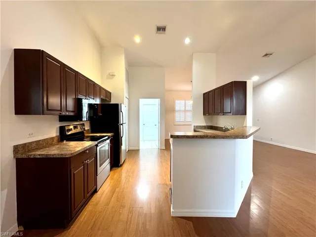 Kitchen featuring dark brown cabinetry, appliances with stainless steel finishes, kitchen peninsula, and light wood-type flooring