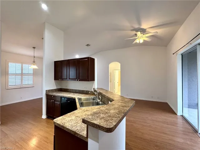 Kitchen featuring vaulted ceiling, kitchen peninsula, sink, black dishwasher, and hanging light fixtures