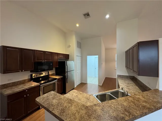 Kitchen with appliances with stainless steel finishes, light hardwood / wood-style flooring, kitchen peninsula, and sink