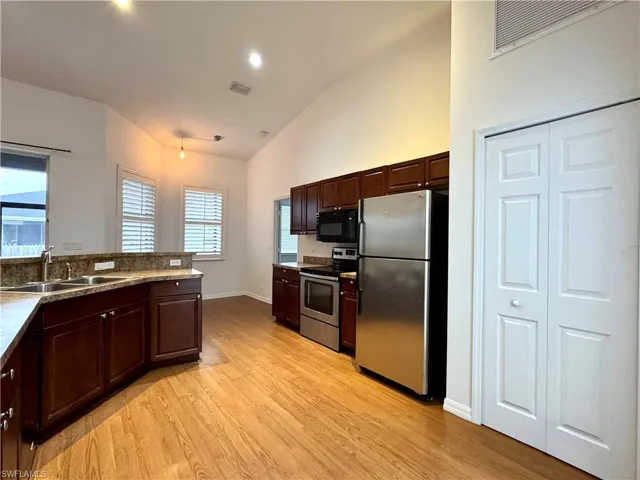 Kitchen featuring stainless steel appliances, lofted ceiling, light hardwood / wood-style flooring, and sink