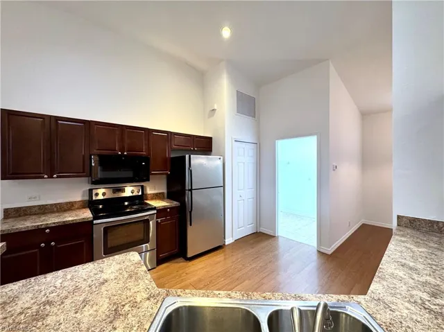 Kitchen featuring appliances with stainless steel finishes, dark brown cabinets, light hardwood / wood-style flooring, and high vaulted ceiling
