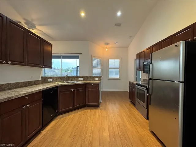 Kitchen featuring dark brown cabinetry, appliances with stainless steel finishes, light wood-type flooring, sink, and vaulted ceiling