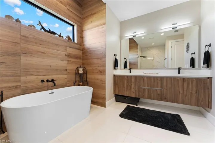 Full bath featuring double vanity, a freestanding bath, light tile patterned flooring, and wooden walls