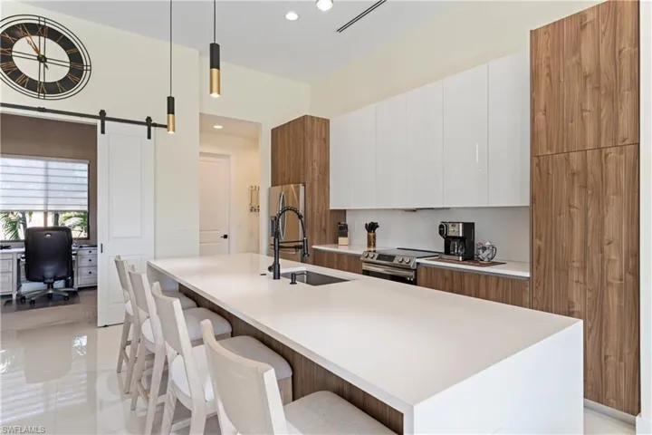 Kitchen with white cabinetry, brown cabinets, modern cabinets, appliances with stainless steel finishes, and decorative light fixtures