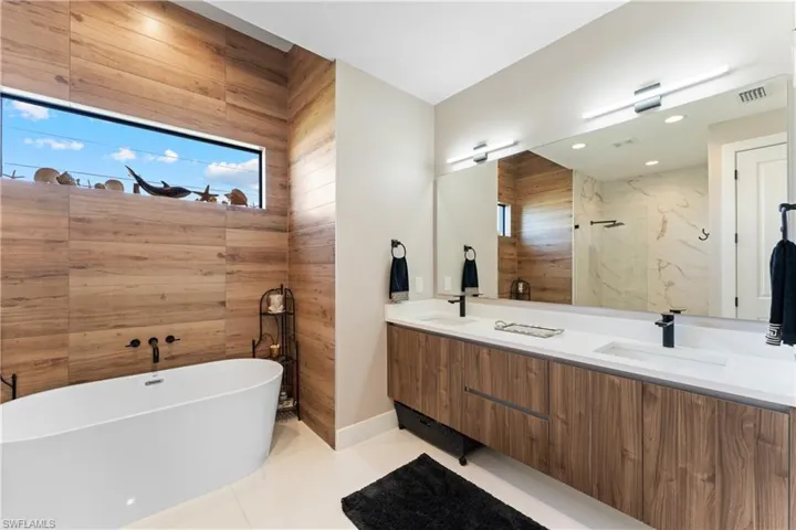 Full bathroom featuring double vanity, a freestanding tub, light tile patterned floors, plenty of natural light, and wood walls