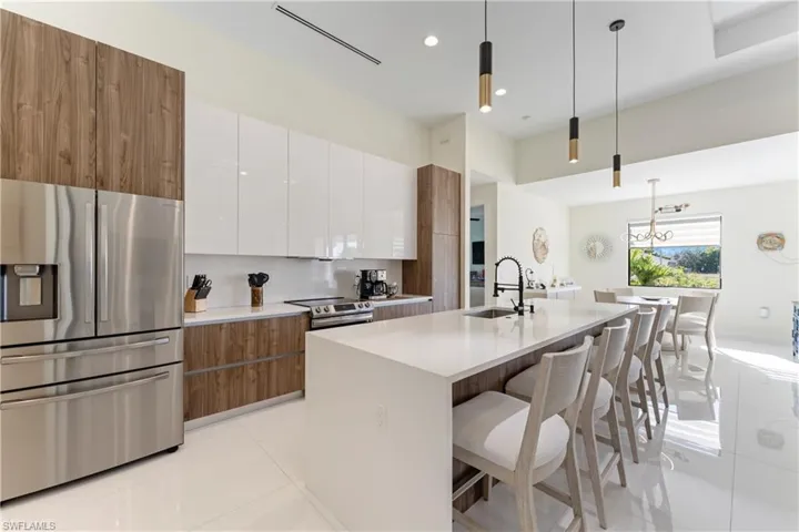 Kitchen with brown cabinetry, white cabinets, appliances with stainless steel finishes, pendant lighting, and modern cabinets
