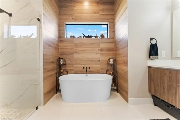 Bathroom with a soaking tub, vanity, tile patterned floors, a marble finish shower, and wooden walls