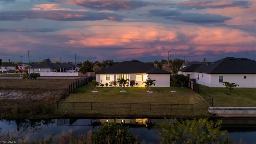 Back of property at dusk with a water view, a fenced backyard, and a patio
