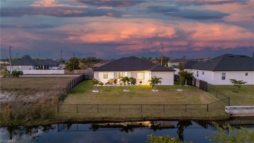 Back of house at dusk featuring a water view, a fenced backyard, and stucco siding