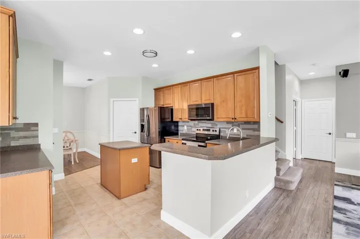 Kitchen featuring a kitchen island, appliances with stainless steel finishes, light wood-type flooring, and decorative backsplash