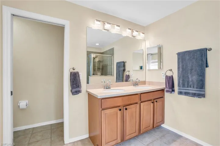 Bathroom with dual vanity, a shower with shower door, and tile patterned floors