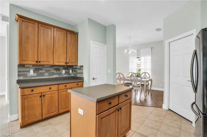 Kitchen with tasteful backsplash, light tile patterned floors, a center island, black fridge, and a notable chandelier